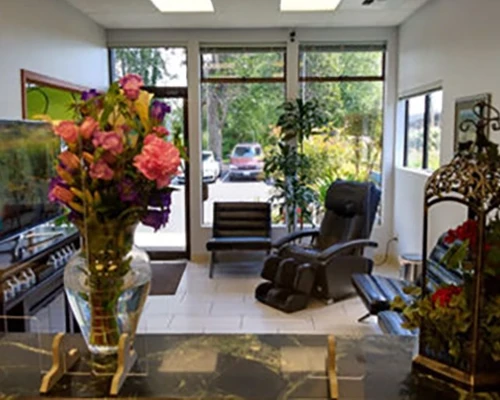 Reception with floral arrangement, seating, large windows, and decorative items near the entrance.