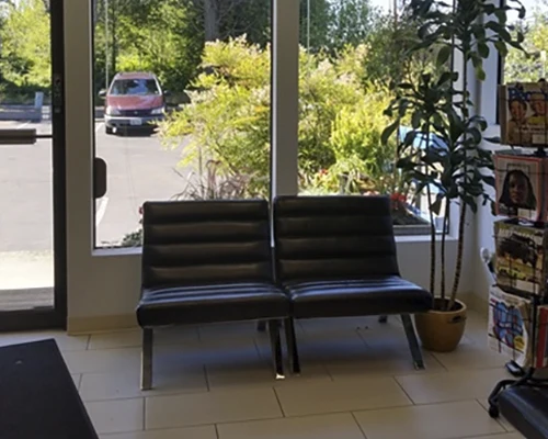 Waiting area near glass entrance with black chairs, magazines, and large front
