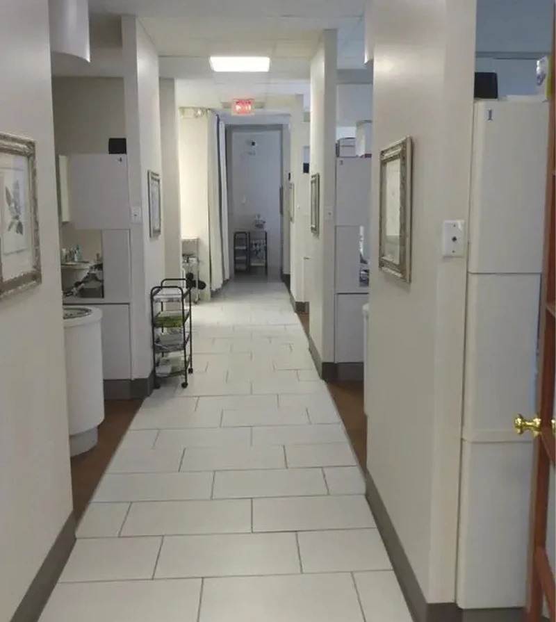 Interior hallway of a dental clinic with tiled floors, framed wall art, and treatment rooms on both sides.