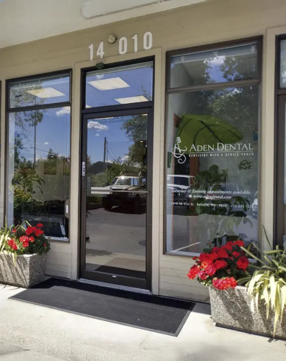 Exterior entrance of a dental office with glass doors, window signage, and flower planters outside.